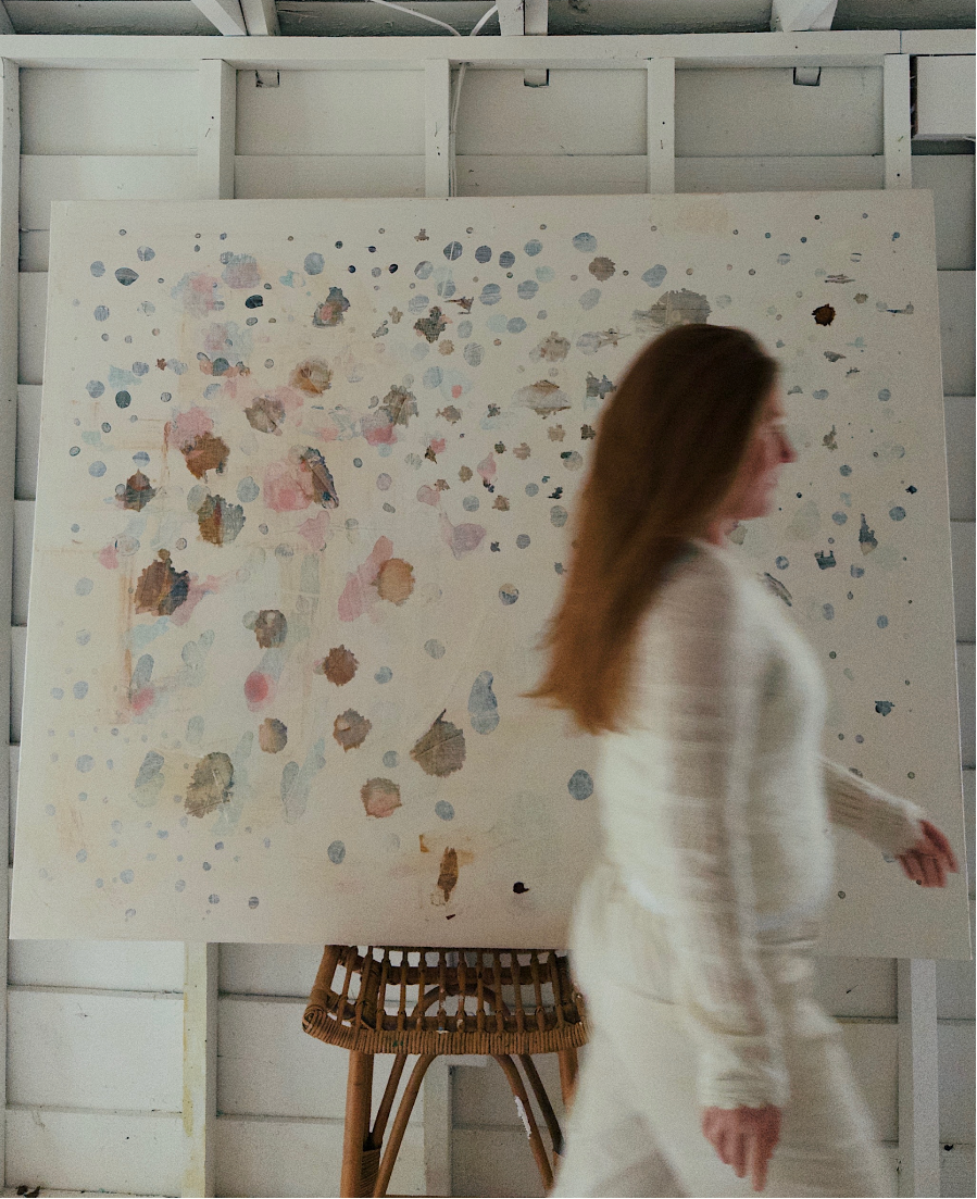 Woman standing in front of a large abstract painting in a white room.